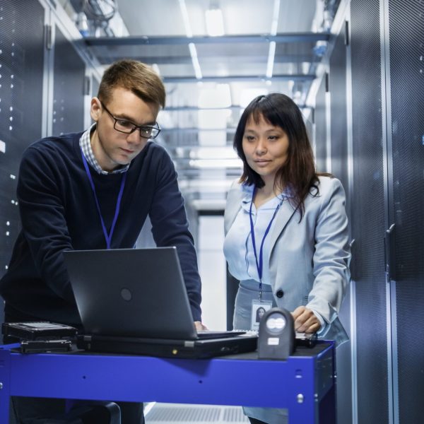 Caucasian Male and Asian Female IT Technicians Working with Computer Crash Cart in Big Data Center full of Rack Servers. Caucasian Male and Asian Female IT Technicians Working with Computer Crash Cart in Big Data Center full of Rack Servers.